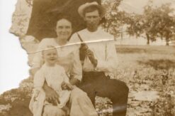 An old photo of a young white couple sitting under an umbrella with their baby.