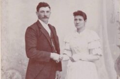 An old photo of a white couple holding hands, a man wearing a dark suit, a woman wearing a white dress.